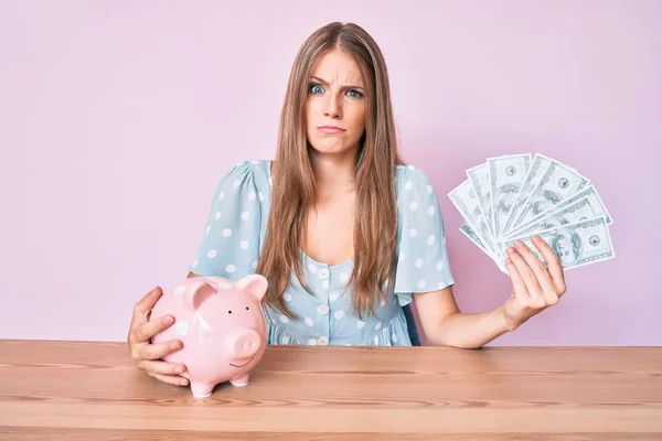 Chica Rubia Joven Sosteniendo Dólares Alcancía Sentado Mesa Escéptico Nervioso — Foto de Stock