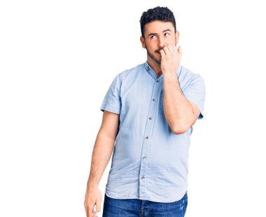 Günlük kıyafetler giyen genç İspanyol adam gergin ve gergin görünüyor. Ağzı tırnak yiyen eller. anksiyete. 