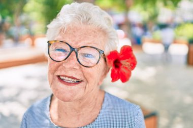 Yaşlı yaşlı, gri saçlı, dışarıda mutlu gülümseyen, dekoratif bir çiçek takan yaşlı kadın.