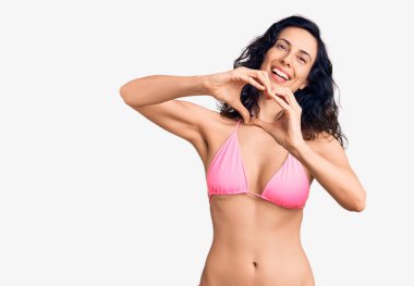 Bikini giyen, aşık gülümseyen ve elleriyle kalp sembolü yapan genç, güzel İspanyol bir kadın. romantik kavram. 