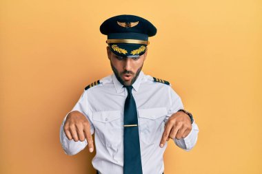 Yakışıklı, İspanyol üniformalı, uçak pilotu üniforması giyen, parmaklarını göstererek reklamını yapan, şaşırmış ve ağzı açık bir adam. 