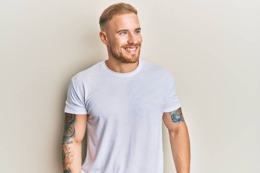 Beyaz tişört giyen, rahat bir görünüm takınan, doğal yüzlü ve kendinden emin bir gülümseme takınan beyaz bir genç.. 