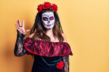 Sarı üzerine ölü kostümü giymiş genç bir kadın beş numarayı gösterip gülümserken kendinden emin ve mutlu bir şekilde işaret ediyor.. 