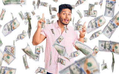 Yakışıklı Latin Amerikalı rahat bir yaz tişörtü giymiş şaşkın şaşkın ve şaşkın bir şekilde parmaklarını kaldırıp kollarını kaldırmış..