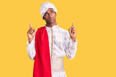 Gelenek giyinmiş Afrikalı yakışıklı bir adam Sherwani sari elbisesi giymiş üzgün ve üzgün görünüyor, parmaklarıyla yönü gösteriyor, mutsuz ve depresif.. 