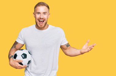 Genç İrlandalı adam elinde futbol topu tutarak zaferi kutluyor. Mutlu bir gülümseme ve kaldırılmış ellerle kazanan bir ifade. 
