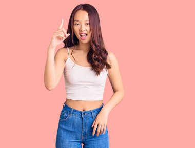 Gündelik giysiler giyen genç, güzel Çinli kız başarılı bir fikri işaret ediyor. Heyecanlı ve mutlu. Bir numara.. 