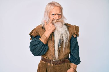Gri saçlı, uzun sakallı, Viking kostümü giyen yaşlı bir adam. Gözüne işaret ediyor. Jestini izliyor. 