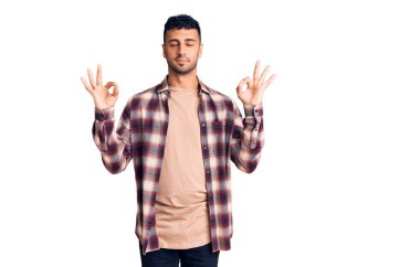 Günlük kıyafetler giyen genç İspanyol adam rahatla ve gözleri kapalı gülümse parmaklarıyla meditasyon hareketi yapıyor. yoga konsepti. 