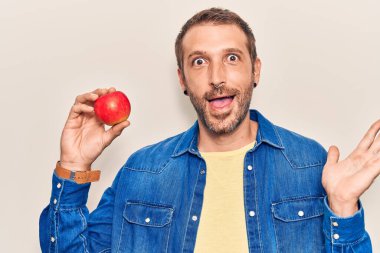 Kırmızı elmayı tutan yakışıklı genç adam başarıyı mutlu bir gülümsemeyle kutluyor ve kazanan yüz ifadesini kaldırıyor. 