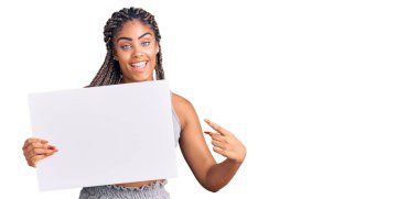 Saçları boş afiş tutan genç Afro-Amerikalı kadın mutlu bir şekilde eli ve parmağı ile işaret ediyor. 