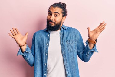 Gündelik giysiler giyen genç bir Arap, habersiz ve kolları açık, hiçbir fikrim yok ve şüpheli bir yüzüm var.. 