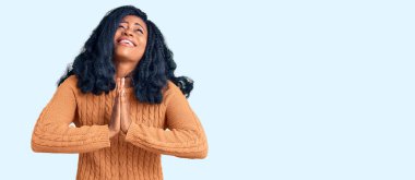 Güzel Afro-Amerikalı kadın, sıradan bir süveter giyer, elleri bağlı yalvarır ve dua eder. Yüzünde umut ifadesi var. Çok duygusal ve endişeli. Yalvarıyor. 