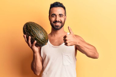 Karpuz tutan genç İspanyol adam mutlu ve pozitif gülümsüyor, başparmağıyla mükemmel ve onay işareti yapıyor. 