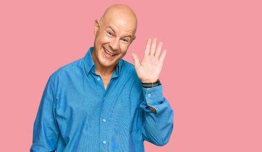 Orta yaşlı, kel bir adam. Günlük kıyafetlerini giyiyor. Merhaba diyor, mutlu ve gülümsüyor. 