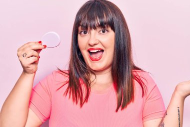 Makyaj süngeri tutan genç ve cüsseli bir kadın zaferi mutlu bir gülümsemeyle ve kazanan bir ifadeyle kutluyor. 