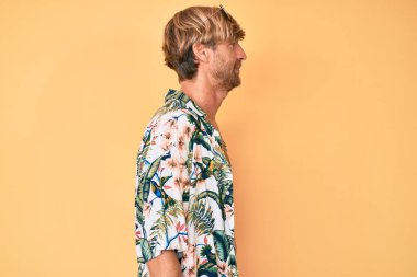 Yaz stili giyinmiş genç sarışın bir adam. Taraf arıyor, rahat poz veriyor. Kendine güvenen bir gülümsemesi var.. 