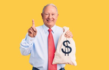 Zarif kıyafetler giymiş, elinde para çantası olan yakışıklı, gri saçlı bir adam bir fikir ya da soru işareti ile şaşırmış, mutlu yüzlü, bir numara 