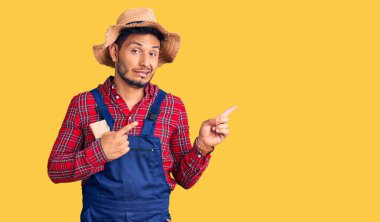 Yakışıklı Latin Amerikalı, giyimli, tamirci üniforması giyen bir yana endişeli ve gergin, endişeli ve şaşırmış bir yüz ifadesi var. 