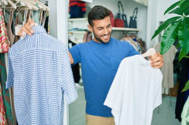 Genç, yakışıklı, gülümseyen, giyim mağazasında giysileri tutan.