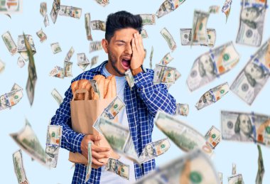 Yakışıklı Latin Amerikalı genç adam elinde kağıt torbayla esneyerek yorgun yüzünü, gözünü ve ağzını eliyle kapatıyor. Yüzüm acıyor..