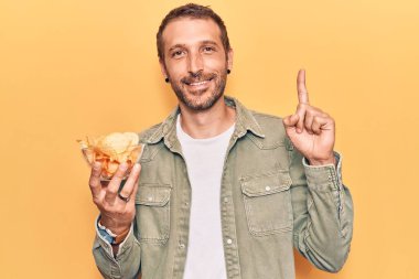Elinde patates cipsi tutan genç yakışıklı bir adam bir fikir ya da soruyla gülümsüyor ve mutlu bir yüzle işaret ediyor. 