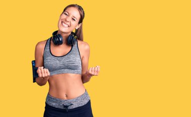 Spor kıyafetleri giyen, kulaklık takan, kolları havada, gözleri kapalı zaferi kutlayan genç, İspanyol bir kadın. Kazanan konsept. 