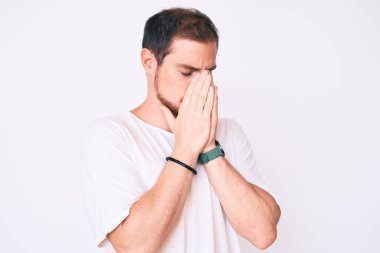 Genç yakışıklı adam, ağlarken suratını ellerle kapatan sıradan beyaz bir tişört giyiyor. depresyon kavramı. 