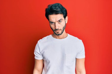 Gündelik beyaz tişört giyen, kuşkucu ve gergin genç İspanyol adam sorun yüzünden surat asıyor. negatif kişi. 