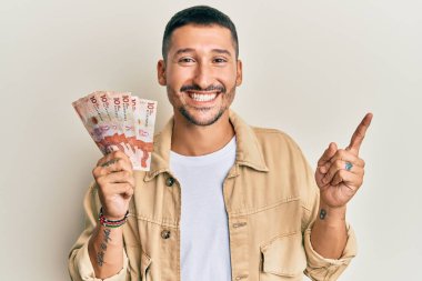 Elinde 10 tane Kolombiya pezosu olan yakışıklı bir adam gülümsüyor. 