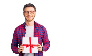 Elinde ayı hediyesi olan yakışıklı genç adam pozitif ve mutlu görünüyor ve kendine güvenen bir gülümsemeyle dişlerini gösteriyor. 