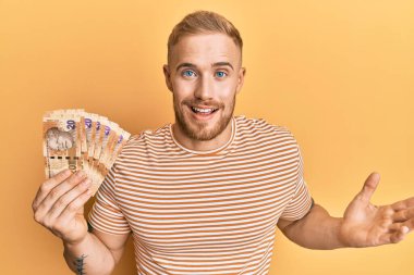 Güney Afrika 'da elinde 20 rand banknot tutan genç beyaz adam başarıyı mutlu bir gülümsemeyle kutluyor ve kazanan ifade elini kaldırıyor. 