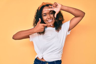 Gündelik kıyafetler giyen, gülümseyen, mutlu yüzlü elleri ve parmakları olan Afro-Amerikan genç bir kadın. yaratıcılık ve fotoğrafçılık kavramı. 