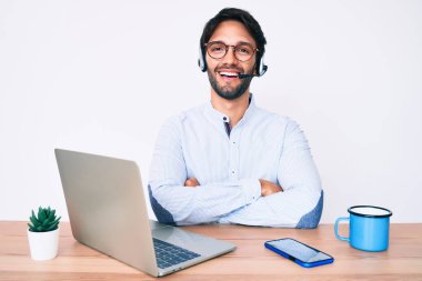 Ofiste çalışan yakışıklı İspanyol adam operatör kulaklığı takıyor ve kollarını kavuşturup kameraya bakıyor. pozitif kişi. 