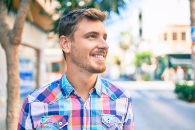 Genç beyaz adam gülümseyerek şehirde mutlu mesut yürüyor..