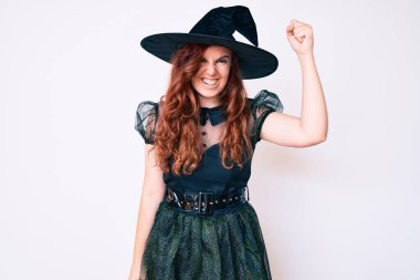 Cadı cadılar bayramı kostümü giyen genç ve güzel bir kadın öfkeyle bağırırken kızgın ve öfkeli bir şekilde yumruğunu kaldırıyor. öfke ve agresif konsept. 