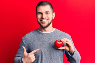 Genç, yakışıklı, kalbi tutan, gülümseyen, mutlu, eli ve parmağı olan bir adam. 