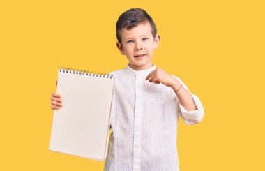 Sevimli sarışın çocuk elinde defterle kendini gösteren mutlu ve gururlu birini işaret ediyor. 