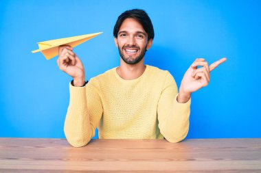 Kağıt uçak tutan yakışıklı İspanyol adam mutlu bir şekilde elini ve parmağını yana doğru uzattı. 