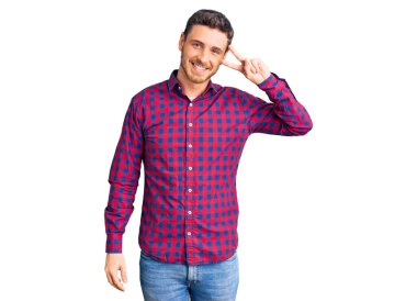 Ayı gömleği giyen yakışıklı genç adam barış sembolü yapıyor. Yüzünde parmakları var. Gülümsüyor, zaferini gösteriyor. 