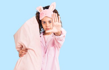 Kıvırcık saçlı, uyku maskesi takan, elinde yastıkla duran, dur işareti yapan, ciddi ve kendine güvenen, savunma jesti olan güzel bir kız. 