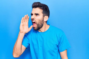 Sakallı, sıradan tişörtlü genç ve yakışıklı bir adam el pençe divan durup bağırıyor. iletişim konsepti. 