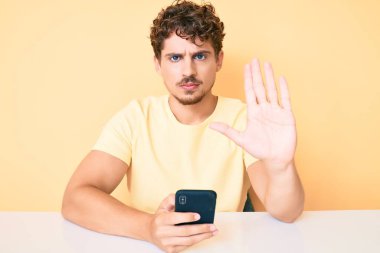 Kıvırcık saçlı, akıllı telefon kullanan, eli açık beyaz bir genç adam dur işareti yapıyor. Ciddi ve kendinden emin bir ifadeyle, savunma jesti. 