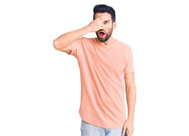 Sakallı, sıradan tişörtler giyen, yüzü ve gözleri kapalı, utangaç ifadesiyle parmaklarının arasından bakan genç yakışıklı bir adam.. 