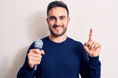 Beyaz arka planda mikrofon kullanarak şarkı söyleyen sakallı yakışıklı genç şarkıcı bir fikir veya soru işareti ile gülümsüyor.