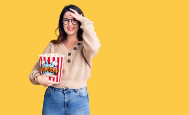 Güzel, genç, esmer bir kadın patlamış mısır yiyor. Stresli ve hayal kırıklığına uğramış, şaşırmış ve kızgın bir yüzü var. 