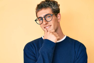 Gündelik kıyafetler ve gözlük takan genç yakışıklı adam kameraya kollarını kavuşturup çenesine dokunarak gülümsüyor. Olumlu düşünmek. 