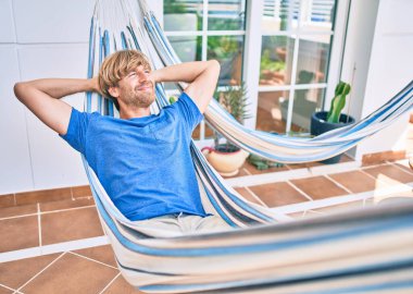 Orta yaşlı yakışıklı bir adam evinin terasında hamakta dinleniyor.