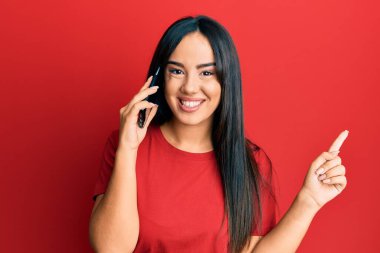 Genç ve güzel İspanyol kız akıllı telefonda konuşuyor gülümsüyor mutlu bir şekilde el ve parmak kenarı işaret ediyor. 