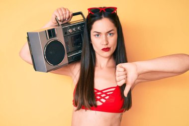 Genç beyaz kadın bikini giyiyor ve elinde kızgın yüzlü teyp var. Eksi işareti baş parmakları aşağıda, reddedilme konsepti reddedildi. 